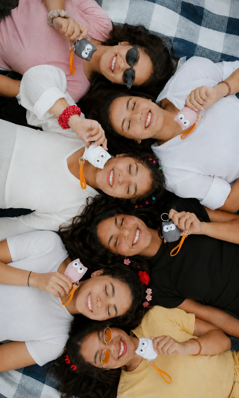 A flock of friends lying in a circle, each holding her Owlie keychain